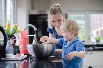 Mother helping son bake cake, son cracking egg