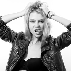 black and white photo portrait of blond young woman beautiful sexy provocative girl in black leather jacket having fun looking at camera touching her head showing tongue on light copy space background