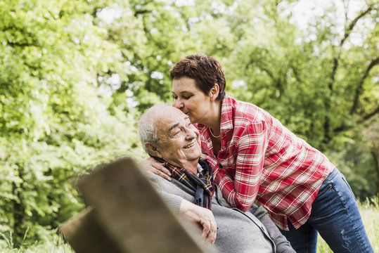 Happy woman kissing her old father sitting on a bench in nature
