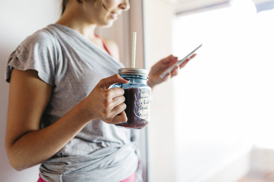 Young woman with healthy drink looking at cell phone