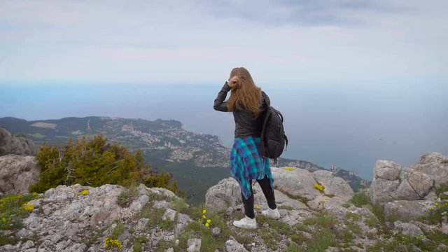 Woman traveler looks at the edge of the cliff on the sea bay of mountains in the background