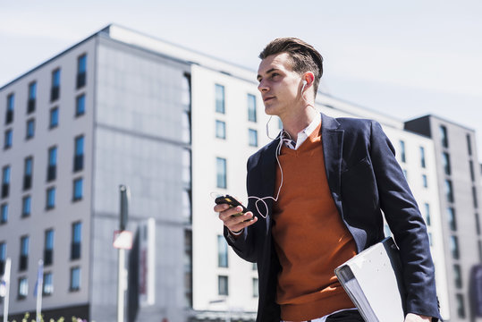 Young man with cell phone, earbuds and folder on the move