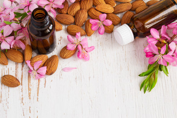 Background with almond oil, almonds and flowers. Top view with c