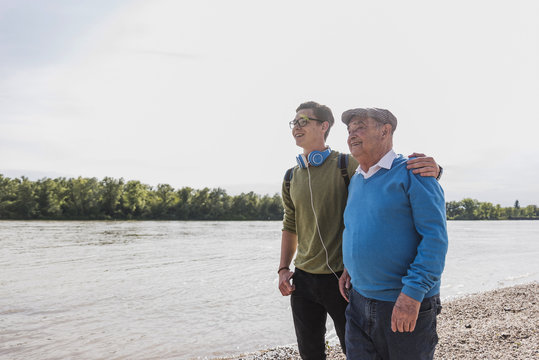 Grandfather and grandson standing at riverside looking together at distance