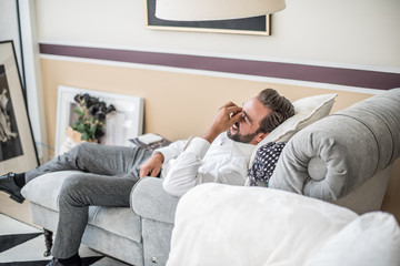 Young businessman reclining and laughing on hotel room chaise longue, Dubai, United Arab Emirates