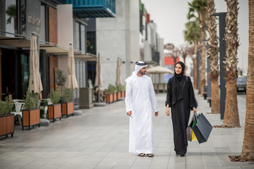 Middle eastern shopping couple  wearing traditional clothing carrying shopping bags, Dubai, United Arab Emirates