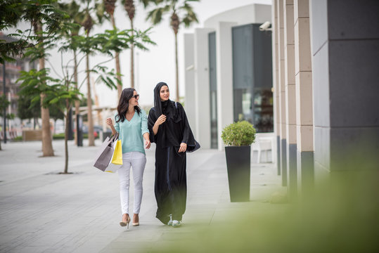 Young middle eastern woman wearing traditional clothing walking along street with female friend, Dubai, United Arab Emirates
