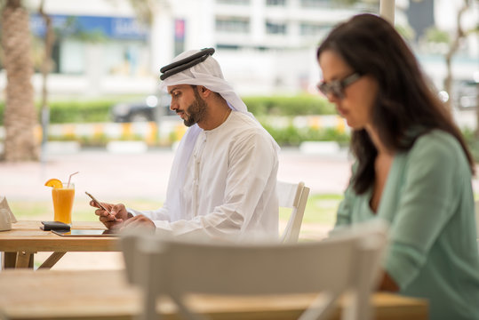 Middle eastern man wearing traditional clothing reading smartphone text at cafe, Dubai, United Arab Emirates