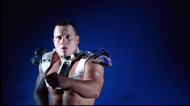 Muscular sexy naked man dancing in the studio on blue light background