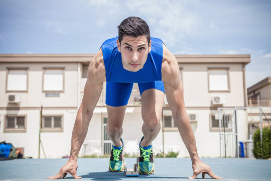 Young male sprinter on his marks on running track