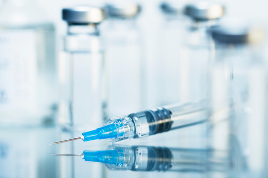 Syringe. Disposable plastic medical syringe surrounded by sealed medication vials