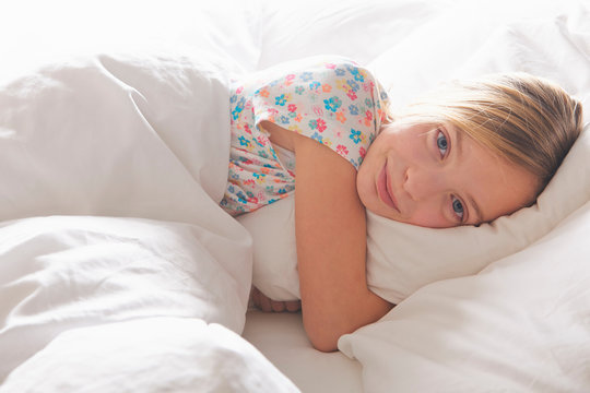 Portrait of blond haired girl hugging pillow in bed