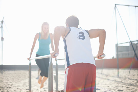 Couple exercising on beach, using gymnastics parallel bars