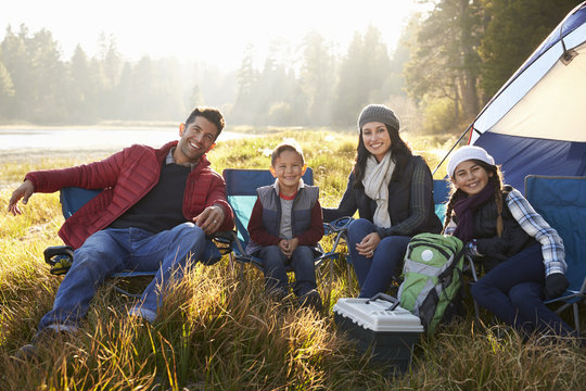 Happy family on a camping trip sit by tent looking to camera