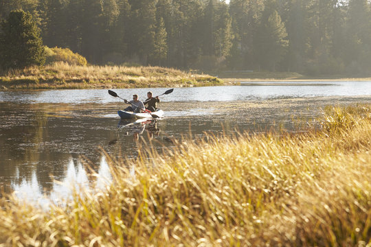 Two young men kayaking on a lake, tall grass in foreground