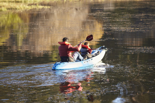 Father and son kayaking together on a lake, back view