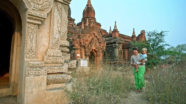 young woman walks carrying toddler son to reach the temple in the ancient Bagan city in Myanmar (formerly Burma)