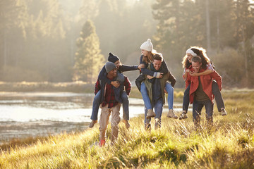 Six friends have fun piggybacking in the countryside by lake