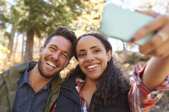 Laughing mixed race couple taking a selfie in a forest