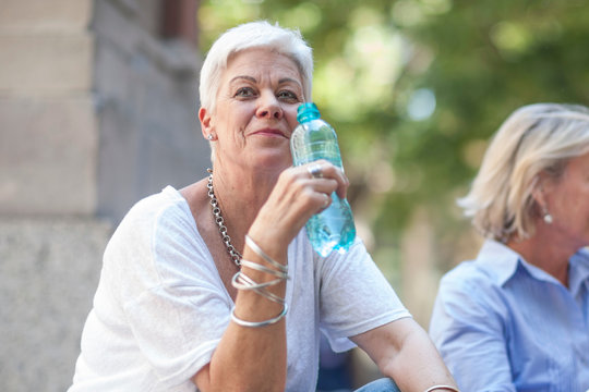 Senior woman sitting with bottle of water in city