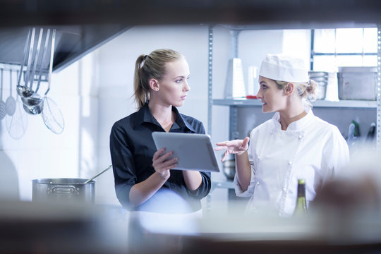 Waitress and chef discussing orders on digital tablet in kitchen