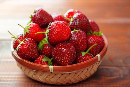 Very beautiful background with fresh strawberries in a wicker round osier basket on old brown wooden background