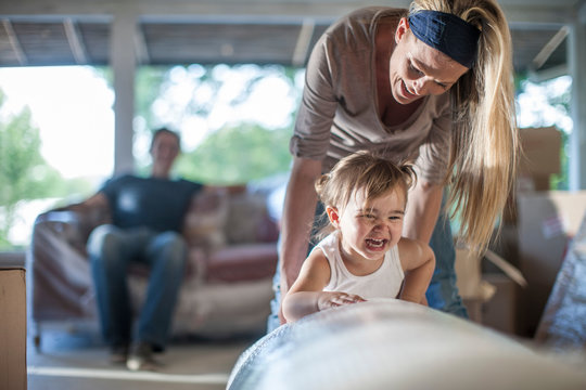Moving house: man sitting on bubble wrapped sofa, woman playing with daughter