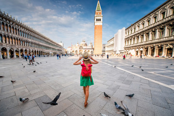 Young female traveler with hat and backpack standing on San Marco square with tower and basilica on...