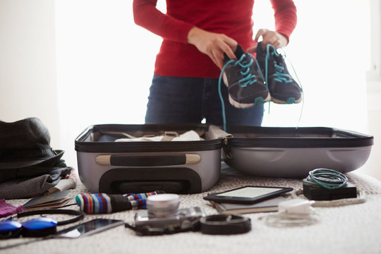Woman packing suitcase, holding trainers, mid section