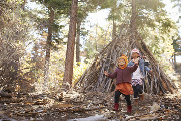 Two girls play outside shelter made of branches in a forest