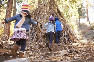 Three kids play outside shelter made of branches in a forest
