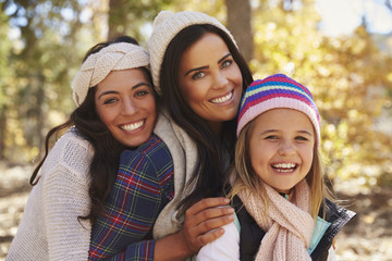 Female parents and daughter in a forest looking to camera