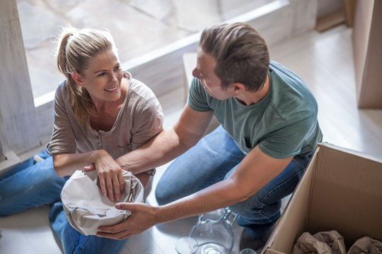 Moving house: couple wrapping glassware in paper before packing