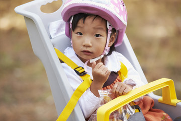 Asian toddler girl in a child bike seat looking to camera
