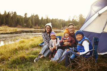 Fototapeta premium Asian family sitting outside their tent, looking to camera