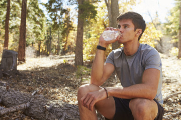 Obraz premium Male runner in a forest takes a break to sit and drink water