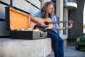 Female street musician sitting on ledge, tuning guitar