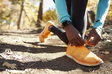 Black female runner in forest tying shoe, low section detail