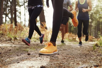 Fotobehang Joggen Benen en schoenen van vier jonge volwassenen die in bos rennen, crop