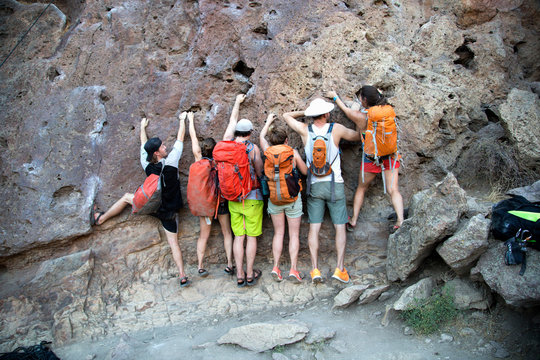Rear view of group of friends side by side clinging onto rock face