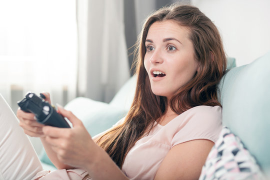 Young woman sitting on couch at home and playing video games