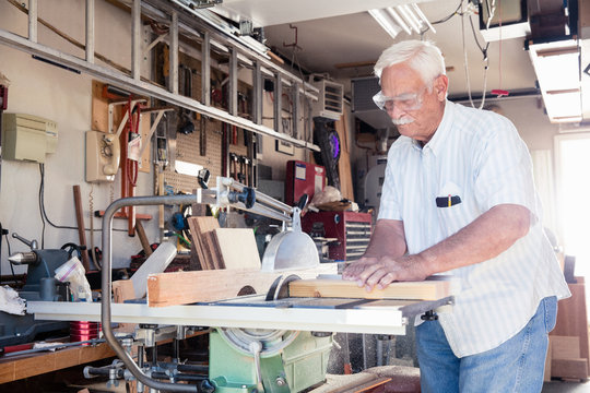 Senior man sawing woodblock on circular saw in carpentry workshop