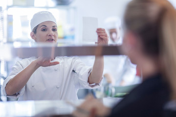 Chef taking orders from waitress in kitchen
