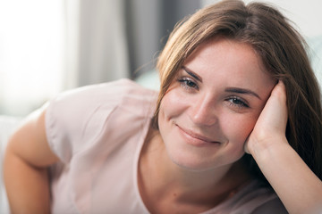 Fototapeta premium Happy young woman lying on couch at home and smiling. Casual style indoor shoot