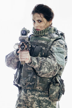 Angry army soldier aiming rifle while standing against white background