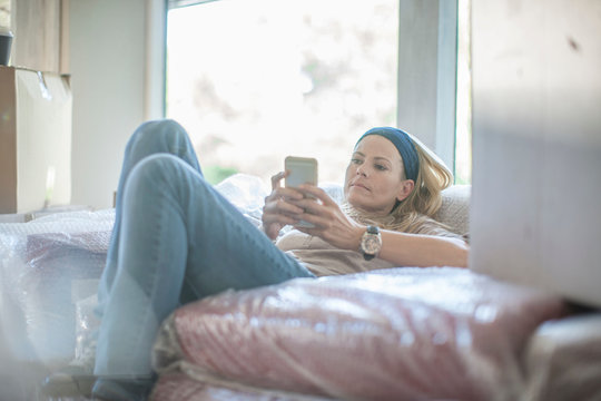 Moving house: woman relaxing on bubble wrapped sofa, using smartphone