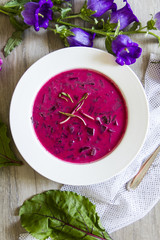 Beetroot, beet leaves soup. White plate, wooden background, flowers.