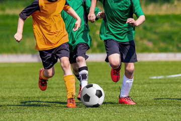 Young boys playing football soccer game on sports field. Running players in colorful green and yellow uniforms. Kids running and kicking soccer ball