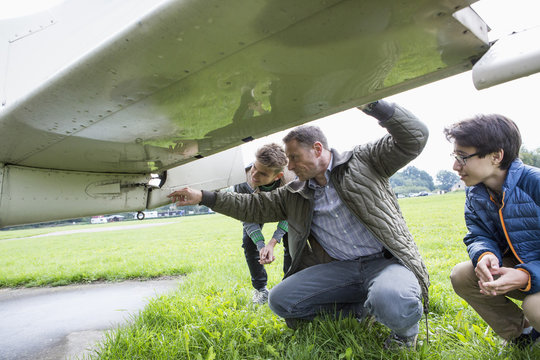 Father explaining airplane parts to sons on field