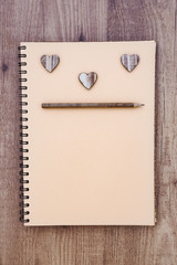 Spiral notebook open with wooden hearts and pencil, on wooden table. Vintage style.